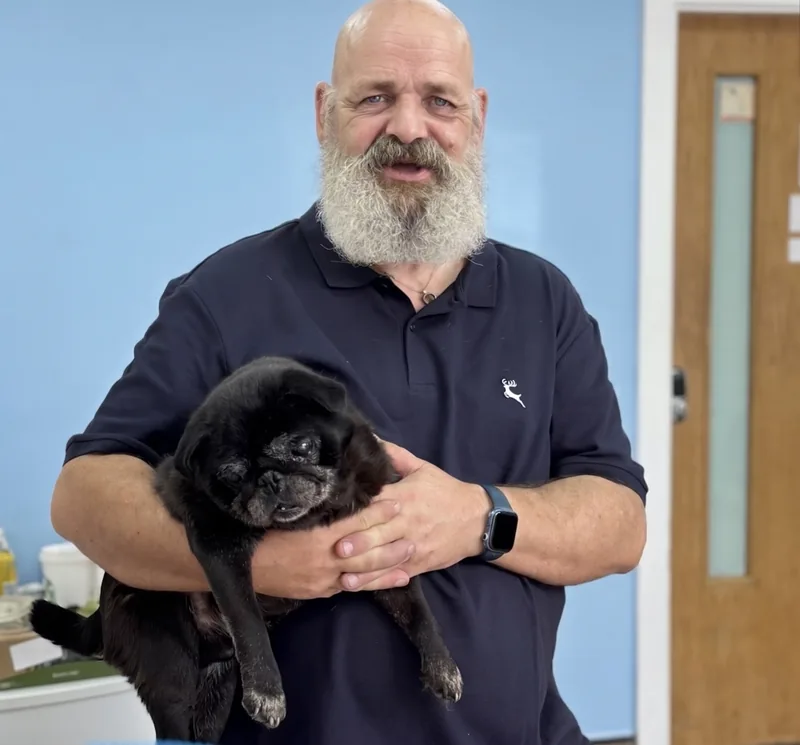 A man gently holding an older black dog